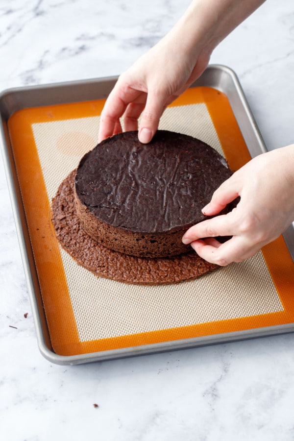 Placing the circle of chocolate cake onto the croustillant base on a silicone mat on a baking sheet.