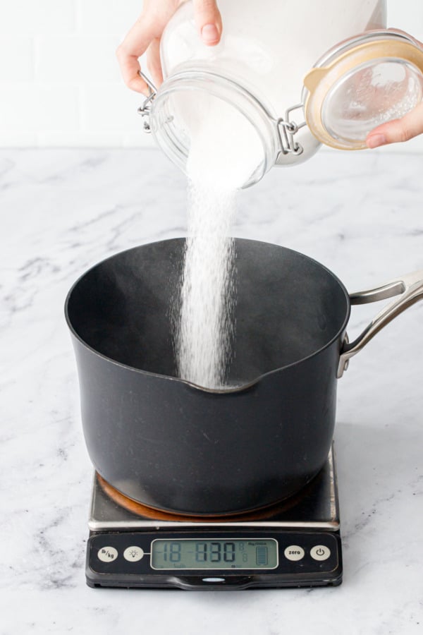 Pouring sugar into a saucepan sitting on a kitchen scale.