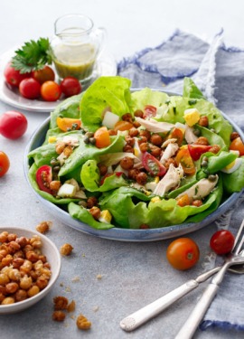 Large shallow dish with butter lettuce and nicoise salad toppings, with a dish of crispy chickpeas and tomatoes and dressing in the background.